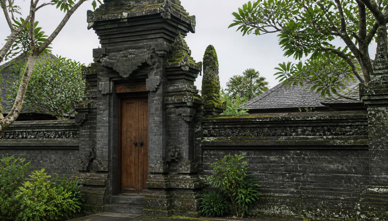 Traditionele Balinese natuurstenen toegangspoort met houten deur en bemoste muur