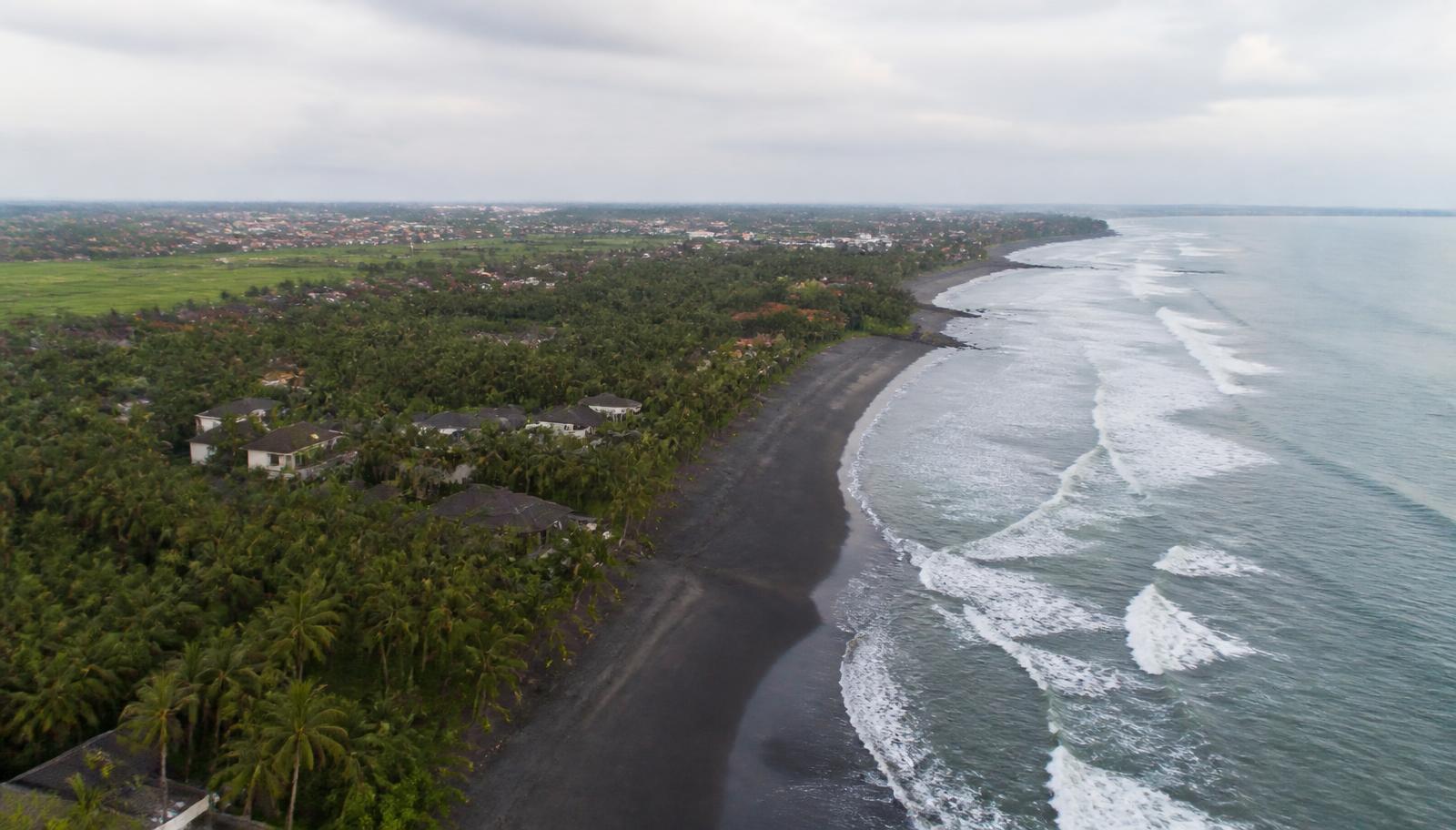 Luchtfoto van de kustlijn bij Canggu met zwart zandstrand, branding en kokospalmen